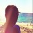 Pixelated image of a person's back with short dark hair, standing on a beach near water under bright sky.