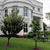 Static pixelated image of a white building with multiple windows, green trees, and a grassy area in front.