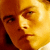 Pixelated close-up of a person's face with warm orange and yellow tones, showing partial facial features including eyes, nose, mouth, and hair against a blurred background.