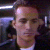 Pixelated static image of a person's face with dark hair and light skin, wearing a white shirt under a dark jacket against a dark background with horizontal light strips.