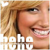 A close-up of a smiling person with light brown hair, showing teeth and a heart symbol in the top-left corner, with the text 'hehe' overlaid at the bottom.