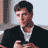 Static pixelated image of a man in formal attire with dark hair and light skin, cropped to show upper body against a neutral background.