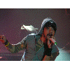 Animated sequence of a person in hooded jacket and cap singing into microphone with hand gestures against dark stage background.