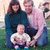 Pixelated group photo of three people standing outdoors on grass with a blurred background, one person holding a child.