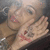 Pixelated image of a person with light skin and dark hair, wearing a brown top, holding an object near their face.