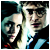 Two pixelated figures in close proximity, one with light hair and the other with dark hair, both facing forward against a dark background.