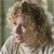Pixelated image of a person with light brown curly hair wearing a light-colored striped shirt against a muted green background.