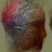 Pixelated image with blurred red, gray, and brown tones forming an indistinct shape against a muted green background.