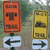 Two vertical rectangular signs with directional arrows below them, one orange and one yellow, set against a blurred green background.