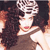 A static pixelated image shows a person with long dark hair wearing a white top and a patterned headpiece, set against a dark background with warm-toned lighting.