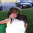 Two people embrace outdoors with a blurred background of grass and vehicles, accompanied by pixelated cyan text on black.