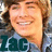 Pixelated close-up of a smiling person with light brown hair wearing a dark blue shirt with large teal letters 'LAC' visible.