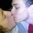 Two people in close proximity, one kissing the other's cheek, wearing striped and maroon clothing against a dark background.