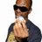 Pixelated image of a person wearing dark sunglasses and a dark jacket, holding a white object near their mouth, with yellow text on black backgrounds.