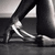 Pixelated grayscale image of a person's lower body wearing dark pants and white sneakers, with one foot lifted in mid-step against a blurred background.