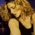 A pixelated image of a woman with curly blonde hair in profile, wearing a black sleeveless top against a dark background.