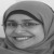 Grayscale pixelated image of a person wearing a hooded garment with a visible headband, smiling with eyes partially closed.
