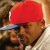 A static pixelated image shows a person wearing a red cap with white trim and dark sunglasses, smiling against a blurred background.