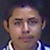 Static pixelated image of a person's face with visible ears, wearing a checkered shirt against a dark background.