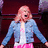 Pixelated image of a person with light hair in a denim jacket and pink pants against blue background text.