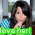 Pixelated image of a person with dark hair holding a finger to lips, green banner with white text 'love her!' at bottom