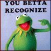 Green frog puppet with red mouth points right under bold text "YOU BETTA RECOGNIZE" on light blue background.