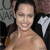 Pixelated image of a person with dark hair tied back, wearing a dark sleeveless top with a white star-like symbol on the shoulder, against a blurred background.