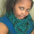 Pixelated image of a person with dark curly hair wearing a blue sleeveless top and teal patterned scarf, looking slightly left.