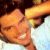 Pixelated close-up of a smiling person with dark hair and light skin, wearing a white top against a blurred background.