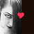 A black-and-white pixelated image of a person's face with closed eyes and long hair, featuring two red heart shapes over the eye areas.