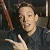 A pixelated static image shows a person with light skin and short brown hair wearing a dark shirt, making a hand gesture with the right hand raised and the left hand extended forward.
