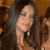 A pixelated close-up of a person with long dark hair, light skin, and a neutral expression against a warm-toned background.