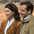Two people stand side-by-side in a pixelated image; the person on the left wears a brown jacket over a white shirt, while the person on the right wears a light-colored jacket over a white shirt.