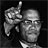 Black-and-white pixelated icon showing a person with glasses pointing upward, rendered in low-resolution grayscale with visible dithering and blocky artifacts.