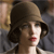 A pixelated close-up of a person wearing a brown wide-brimmed hat with dark hair visible beneath, red lips, and a light-colored garment against a blurred background.