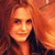 A pixelated portrait of a person with long reddish-brown hair, wearing a dark top, against a warm-toned background with orange and brown hues.