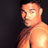 Pixelated static image of a shirtless man with short dark hair against a solid black background, rendered in warm orange and brown tones.