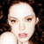 Pixelated close-up of a person with light skin tone, dark brown hair, and pink lips, wearing a white top against a dark background.