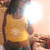 A person in a yellow sleeveless top stands with arms crossed, facing left, against a bright light source and blurred background.