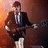 A pixelated image of a person playing an electric guitar, with red and gray background sections containing text.