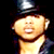 Pixelated static image of a person with light skin tone wearing a dark top hat and brown neckwear against black background, showing upper body from shoulders up.