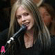 A person with long light brown hair sings into a microphone across six showing different mouth positions and pink letters A, V, R, I, L