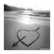 A grayscale beach scene with a heart-and-arrow symbol drawn in sand, paired with blue pixelated text reading "I Love You" on the right side of the image.