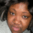 Pixelated close-up of a person's face with light brown skin tone, dark eyes, and short curly hair against a blurred background.