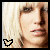 Pixelated close-up of a person with blonde hair and bangs, featuring three distinct heart-shaped icons in the bottom-left corner