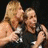 Two people embrace in a wrestling ring with microphones, surrounded by green pixelated text on black and gray backgrounds.