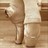A pixelated static image of a figure in light-colored clothing standing against a brown background with vertical lines.