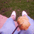 A person in light blue pants and white shoes sits on a pink surface with a small brown object near their feet on green grass.