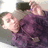 Pixelated static image of a person with light skin tone wearing a dark purple garment and a dark cap, positioned against a light background.