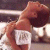 Pixelated image of a person with brown hair wearing a white top, holding a white object with dark text, against a blurred background.